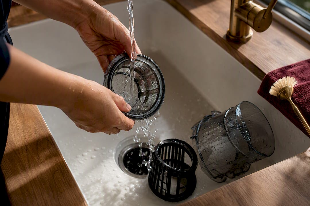 Hands rinsing juicer parts in kitchen sink