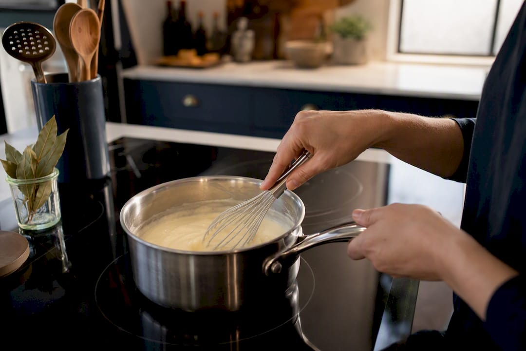 Hands whisking roux in copper saucepan