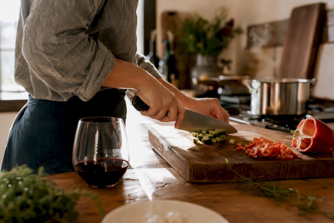Hand slicing vegetables with chef's knife near wine glass