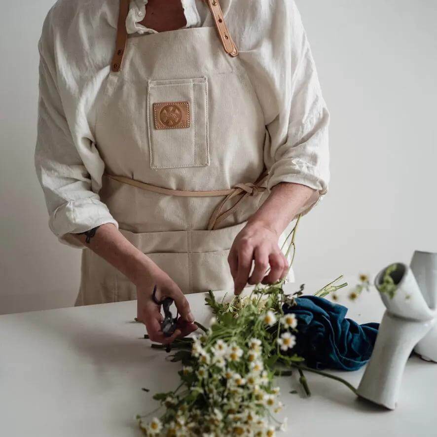 Natural Canvas Apron for Home Cooks worn while arranging flowers on a table, showcasing creativity in home gardening.