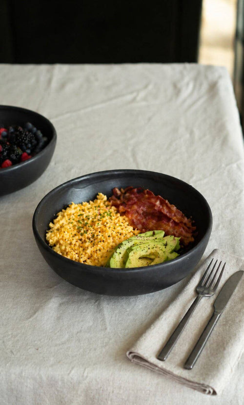 Black Matte Stoneware Pasta Bowl filled with scrambled eggs, bacon, and avocado on a dining table.