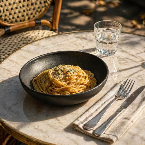 Black Matte Stoneware Pasta Bowl with spaghetti on a marble table, complemented by glass and cutlery.