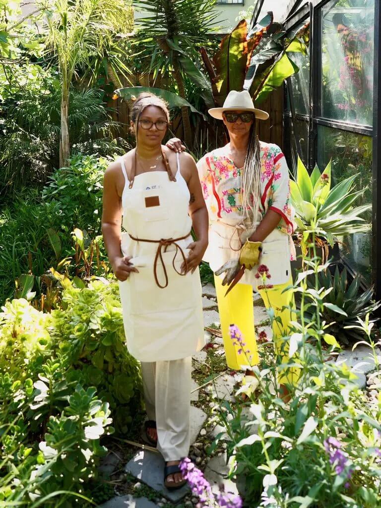 Natural Canvas Apron for Home Cooks Two individuals wearing natural canvas apron in a vibrant garden setting, showcasing gardening style and creativity.