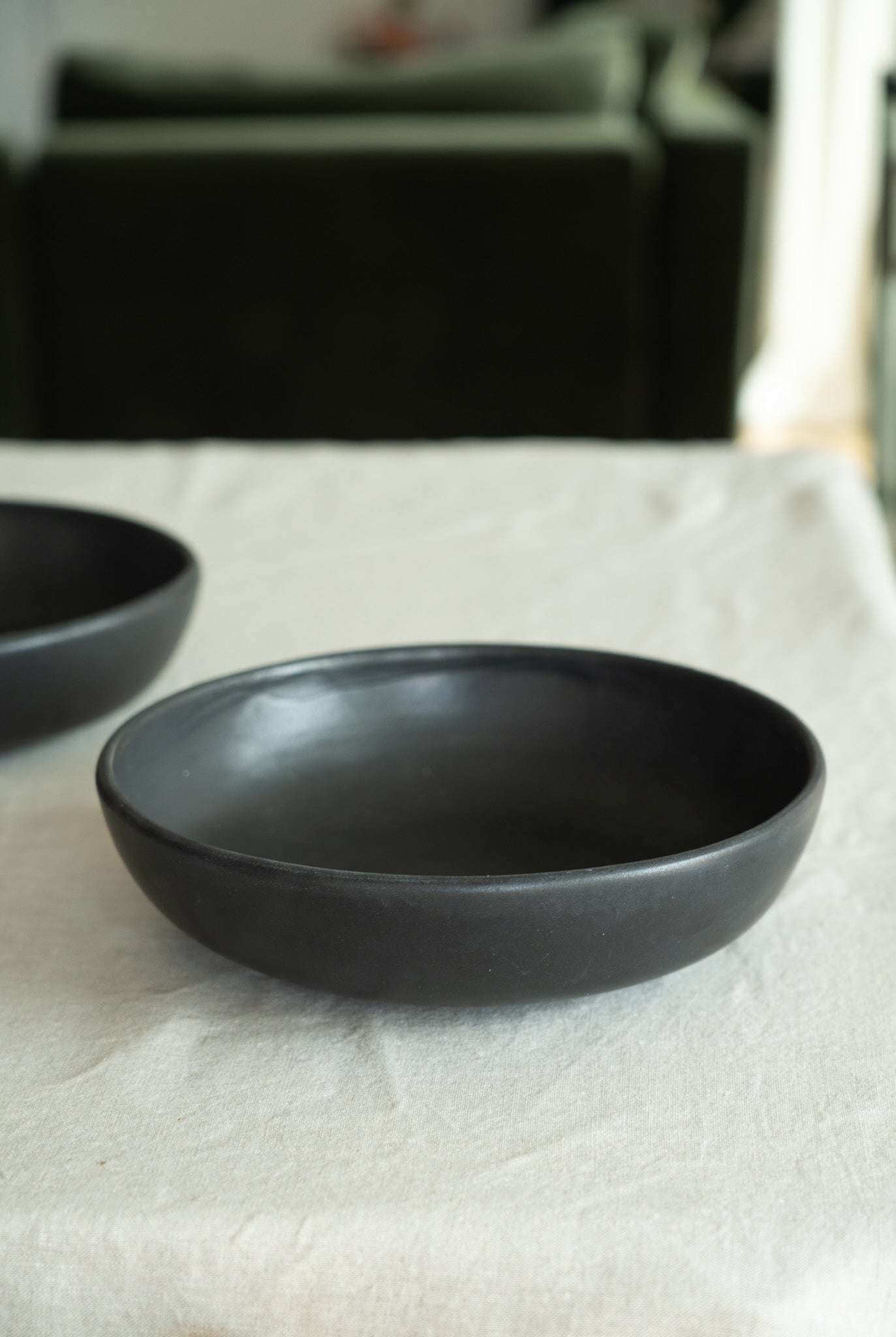 Black Matte Stoneware Pasta Bowl on a linen tablecloth, showcasing its elegant design and versatile use.