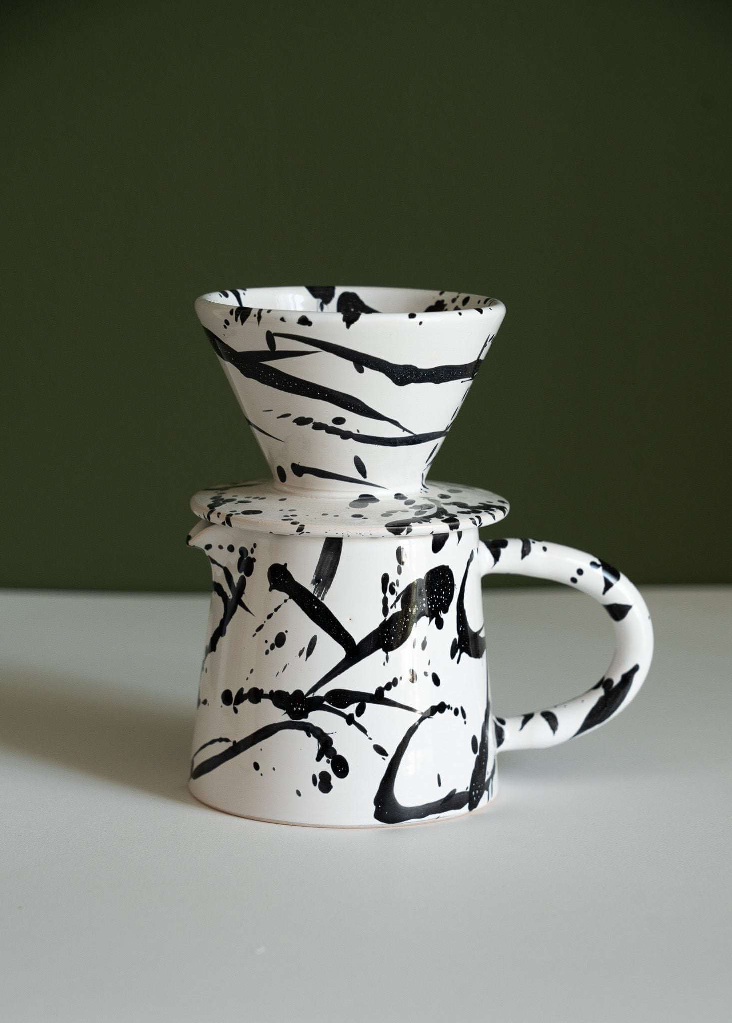 Handmade ceramic pour over coffee set featuring a dripper and pitcher with abstract black and white splatter design.