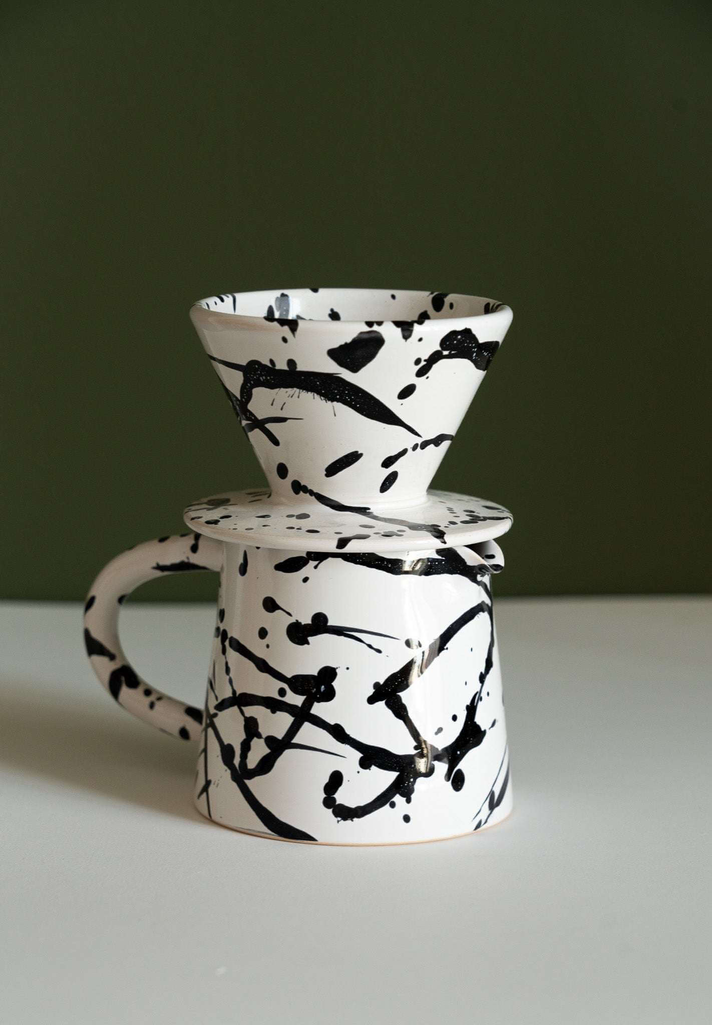 handmade ceramic pour over coffee set featuring a black and white splatter design coffee dripper and pitcher.