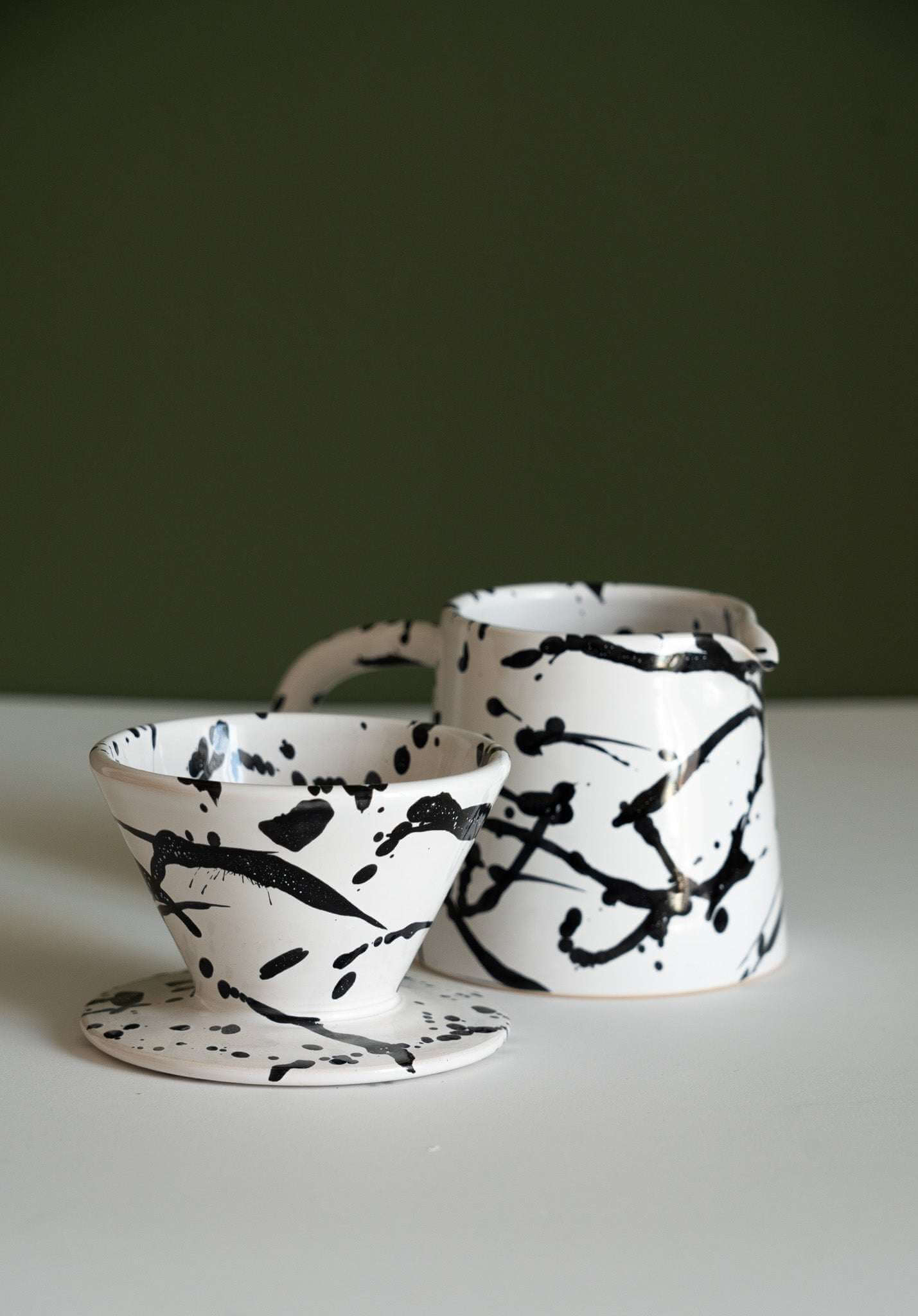 handmade ceramic pour over coffee set featuring a dripper and pitcher with a stylish black and white splatter design.