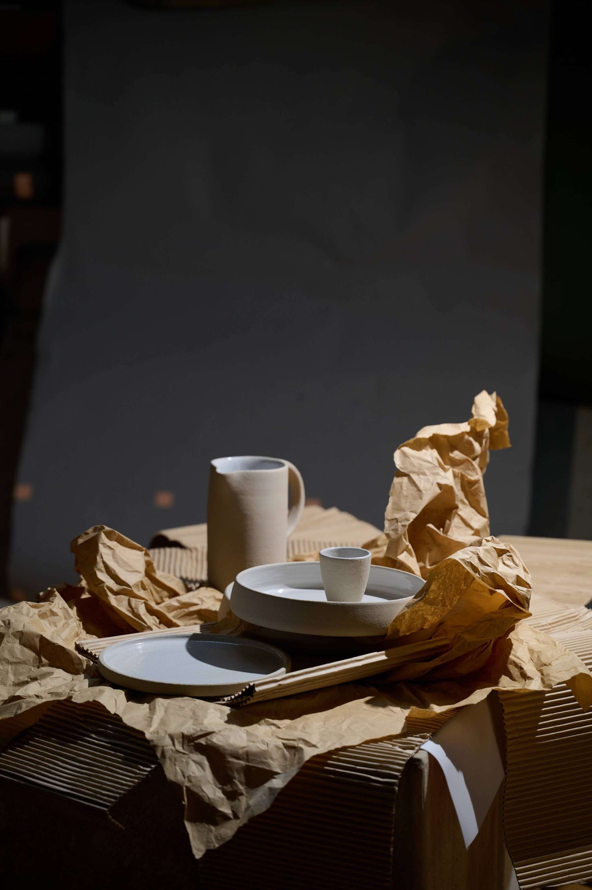 Handmade stoneware dinner plates displayed with a pitcher and wrapped in rustic paper.