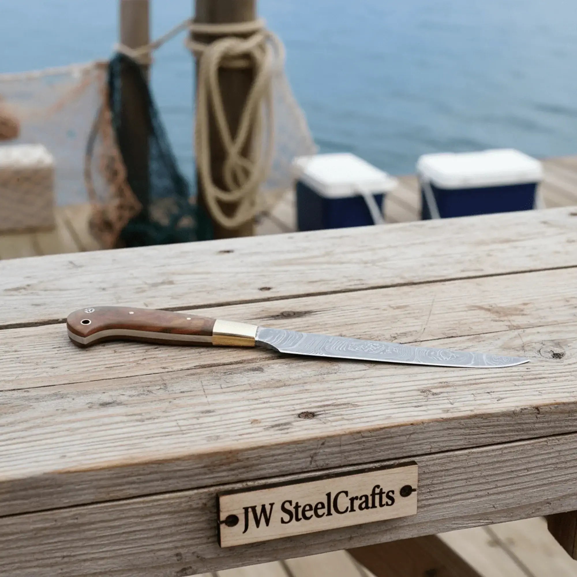 Handmade Damascus fillet knife placed on a wooden table by the water, perfect for fish processing and trimming.