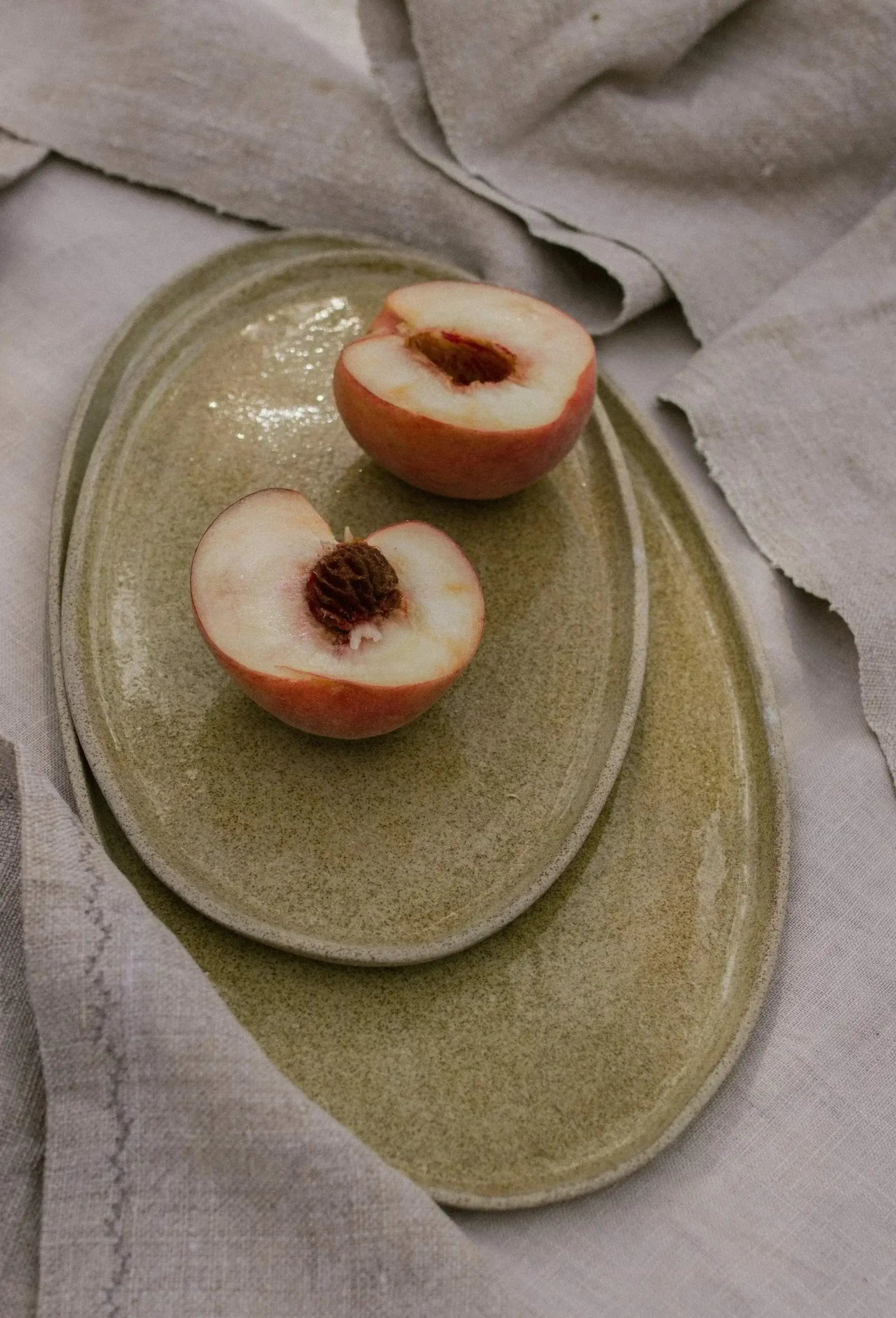 Handmade stoneware serving platter featuring sliced peaches on a rustic table setting.