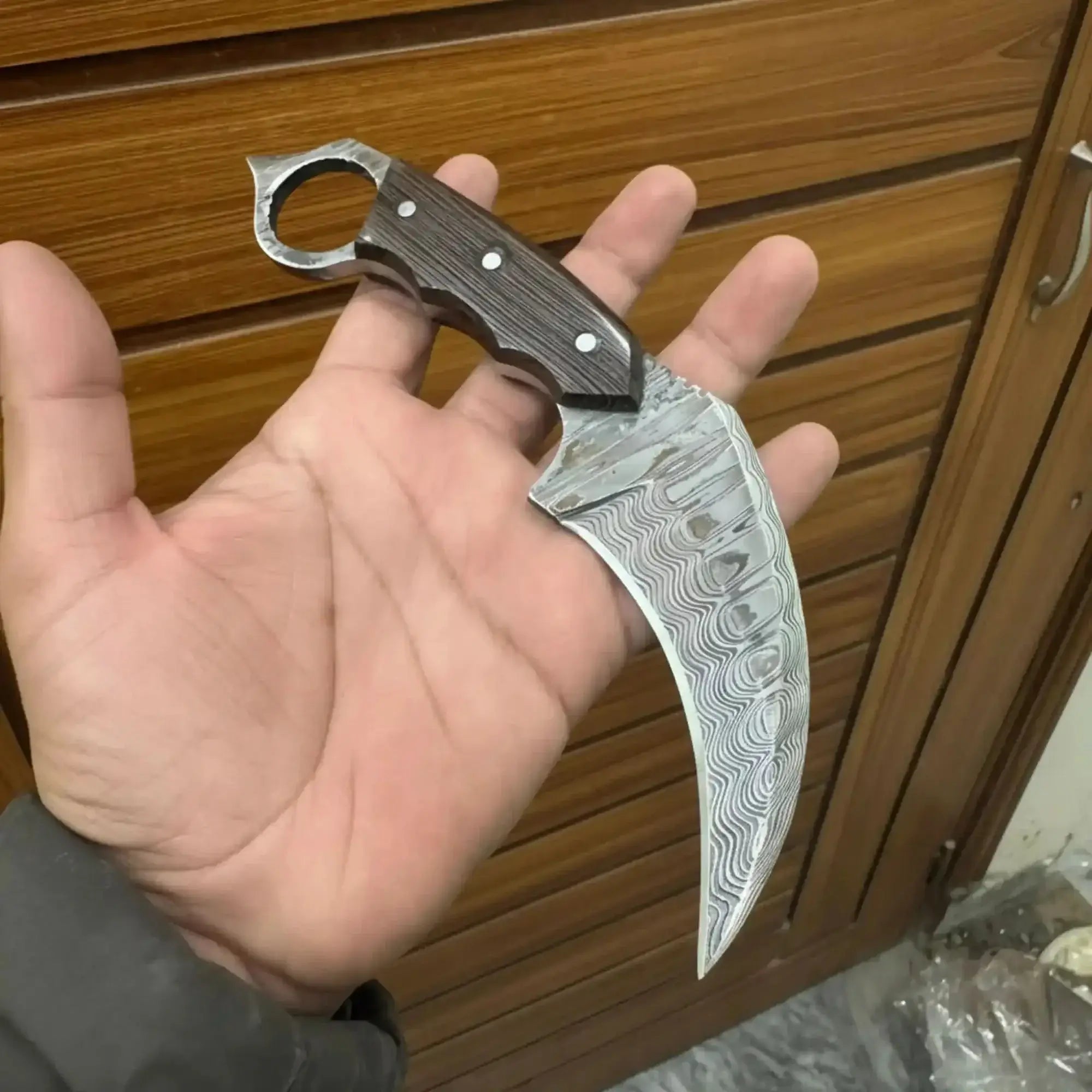damascus hawkbill utility knife held in hand, showcasing curved blade and ring handle design.
