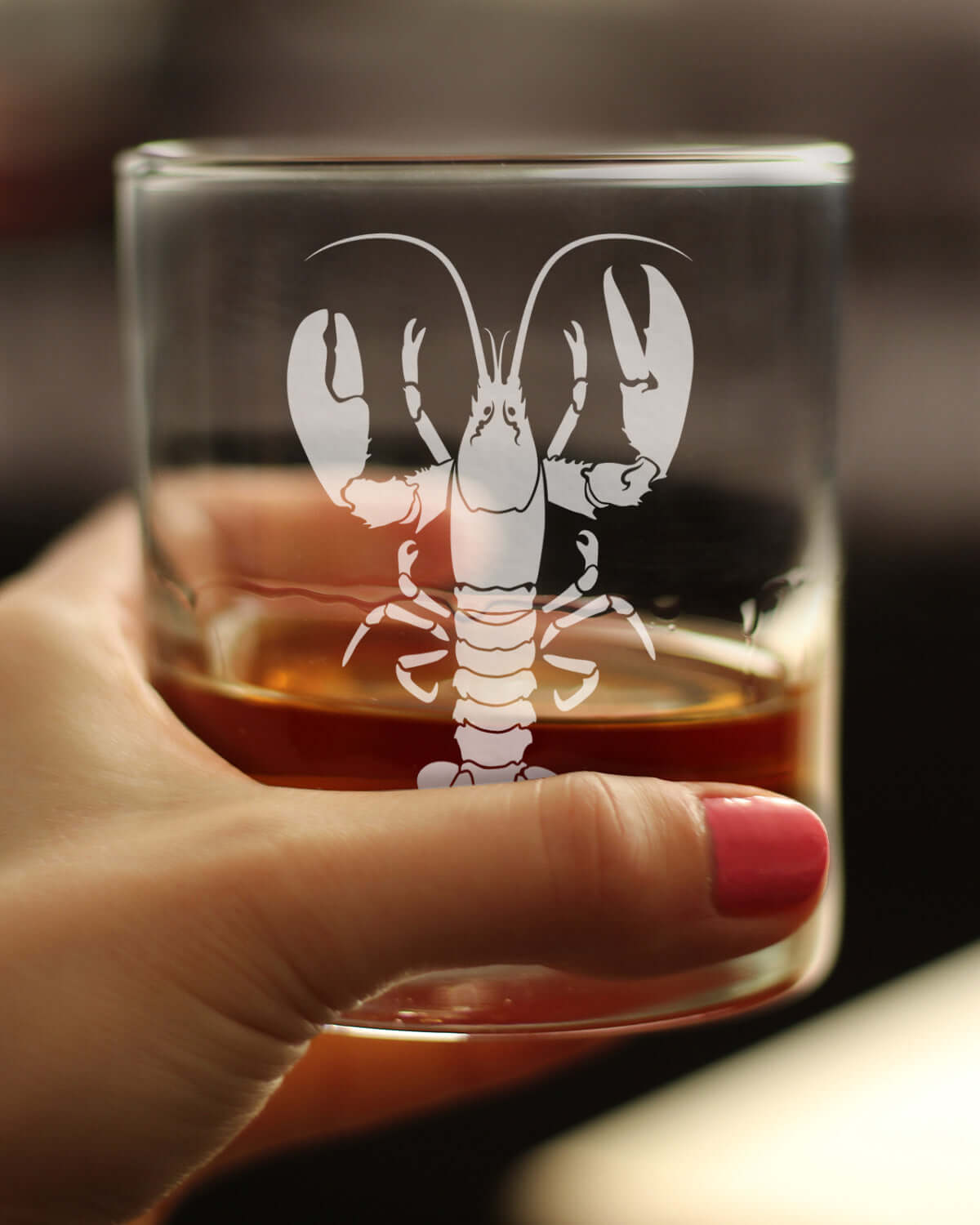 Lobster engraved rocks glass held with whiskey, perfect for coastal decor and unique barware.