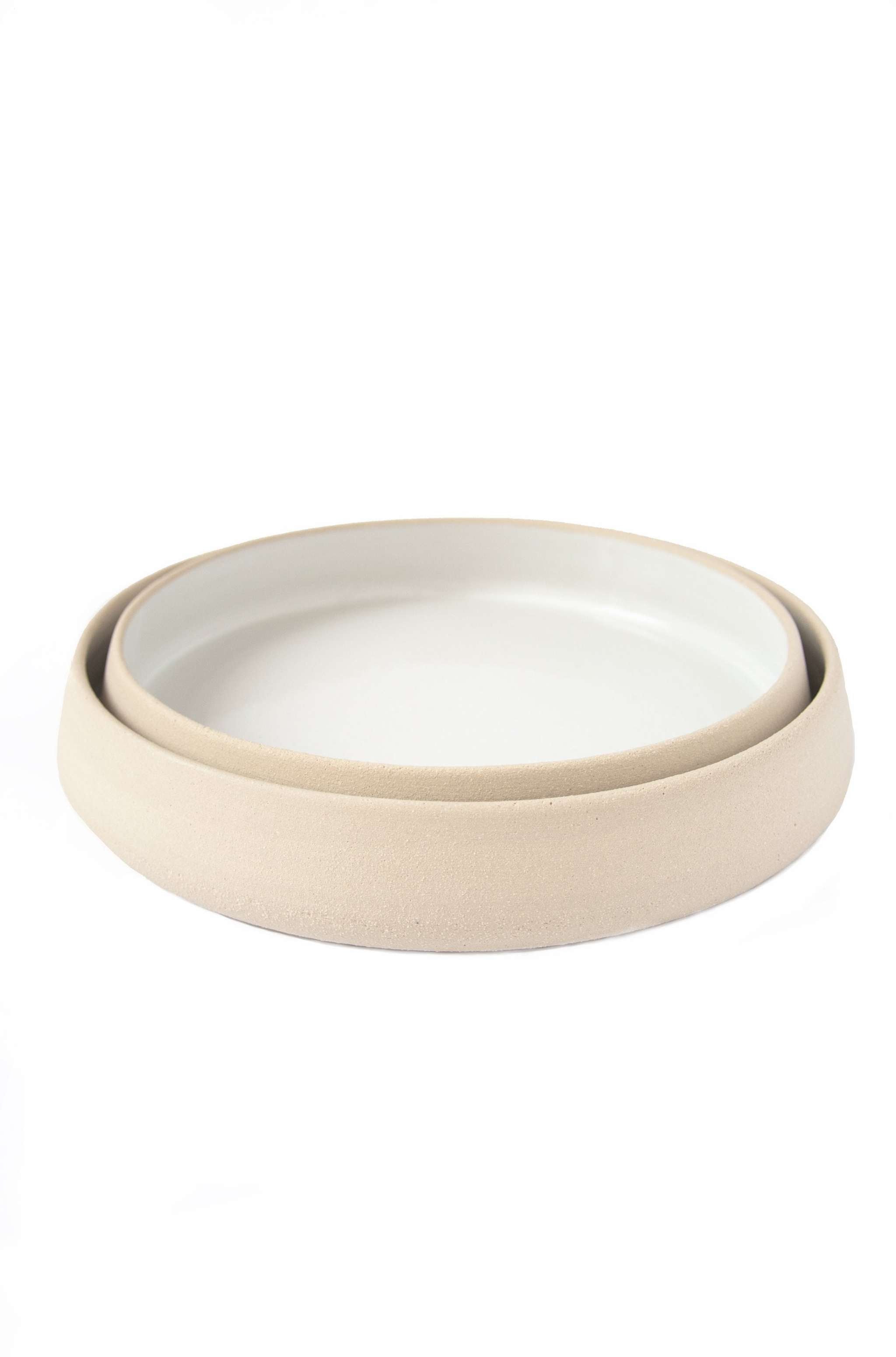 Handmade stoneware dinner plates with high sides showcasing a textured exterior and glossy white interior.
