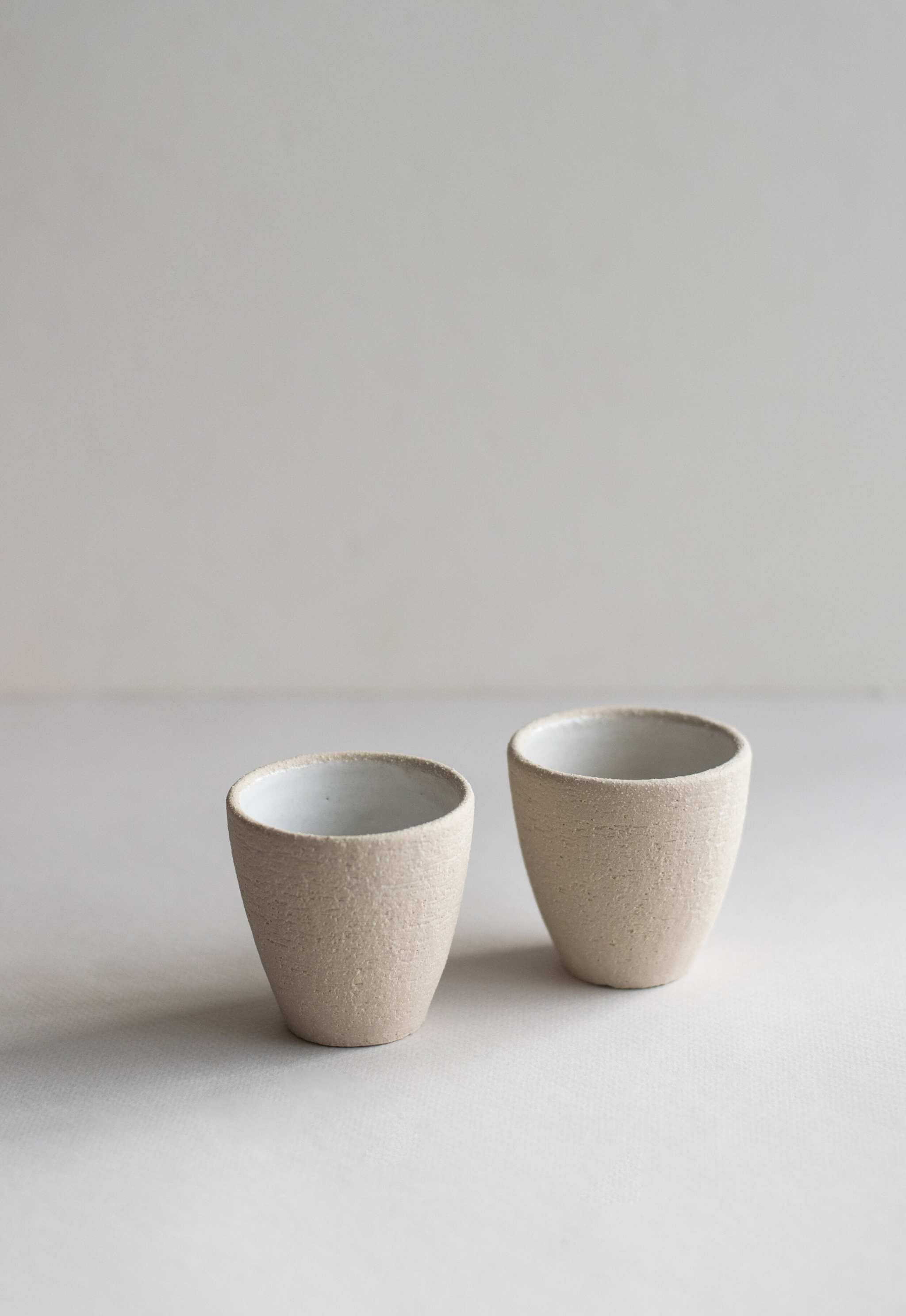 Handmade stoneware espresso cup set with exposed clay exterior and shiny white interior glaze.