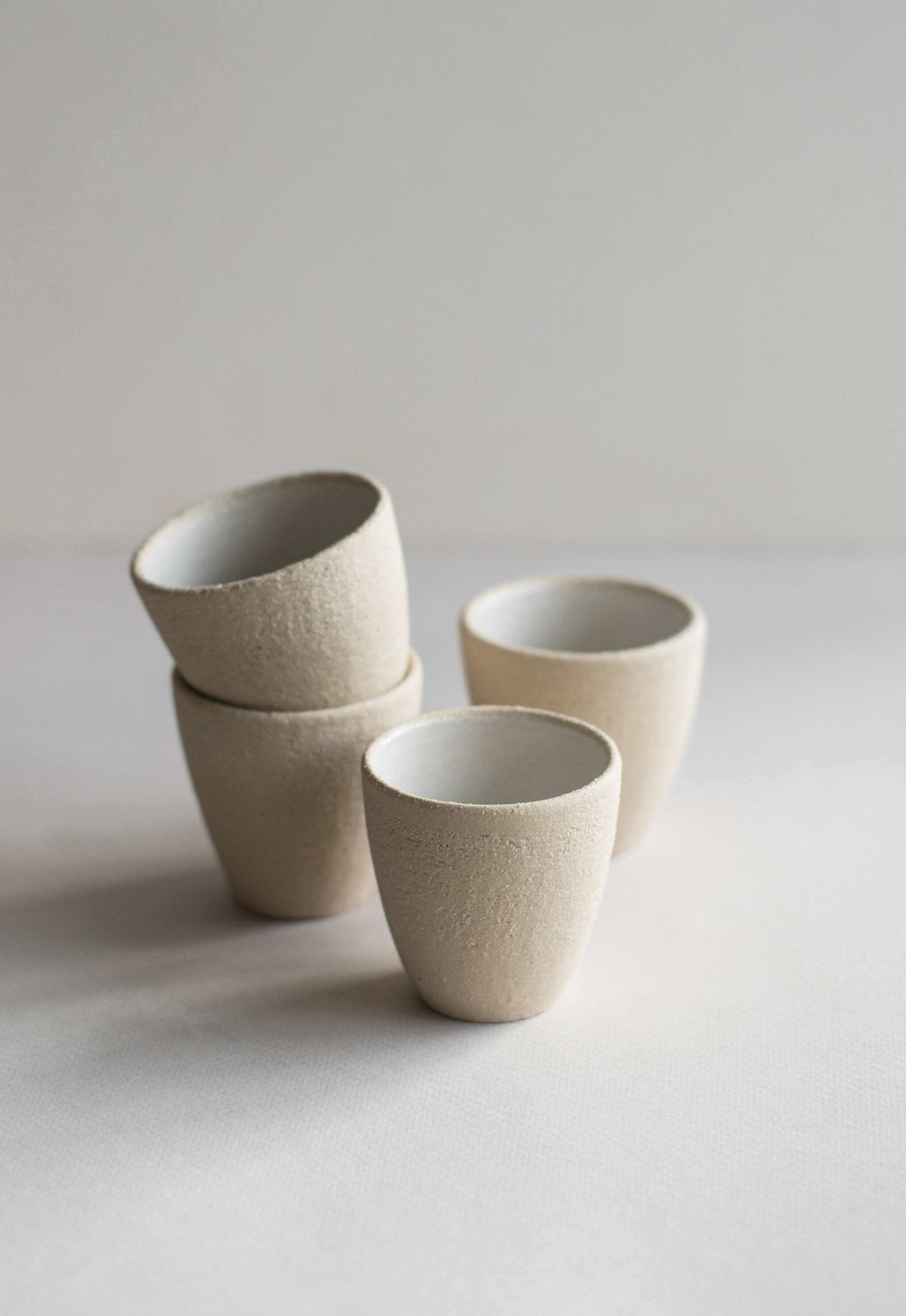 Handmade stoneware espresso cup in a stack, featuring exposed clay texture and white glossy interior.
