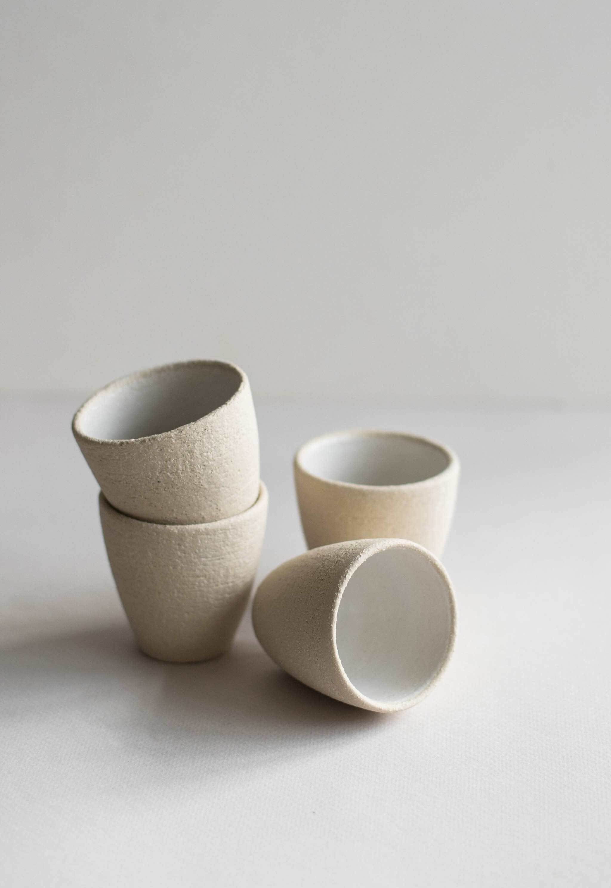 Handmade stoneware espresso cup set in natural clay with white glaze, highlighting unique textures and shapes.