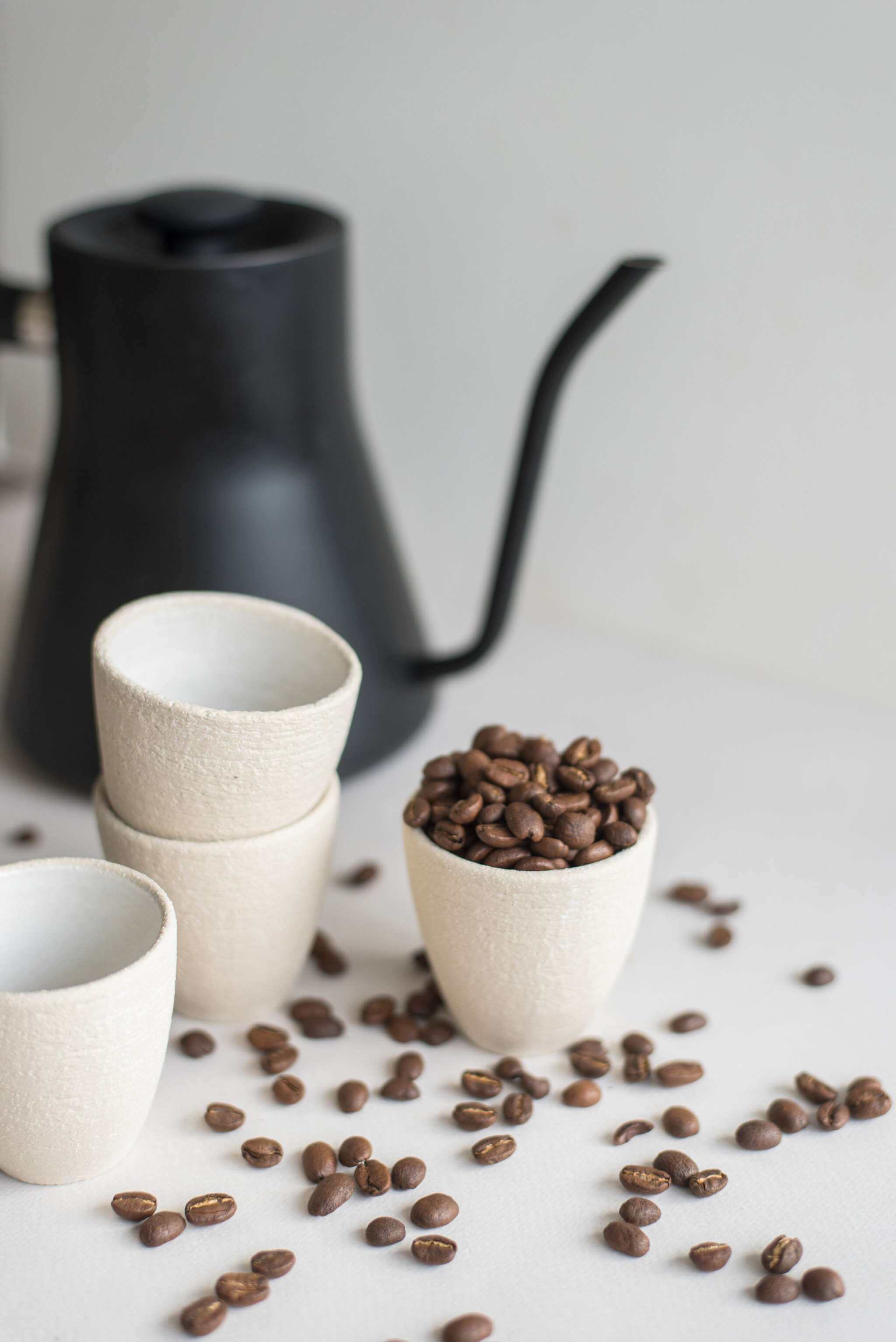 Handmade stoneware espresso cup stacked beside a kettle and coffee beans scattered on the table.