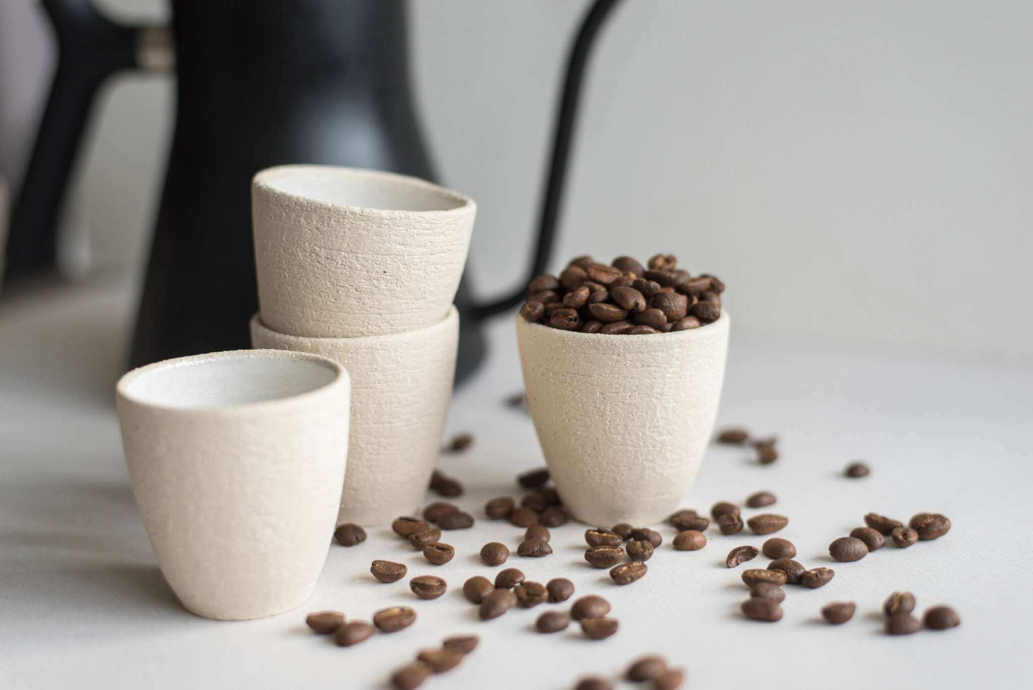 Handmade stoneware espresso cup with coffee beans, showcasing rustic texture and elegant design in a cozy setting.
