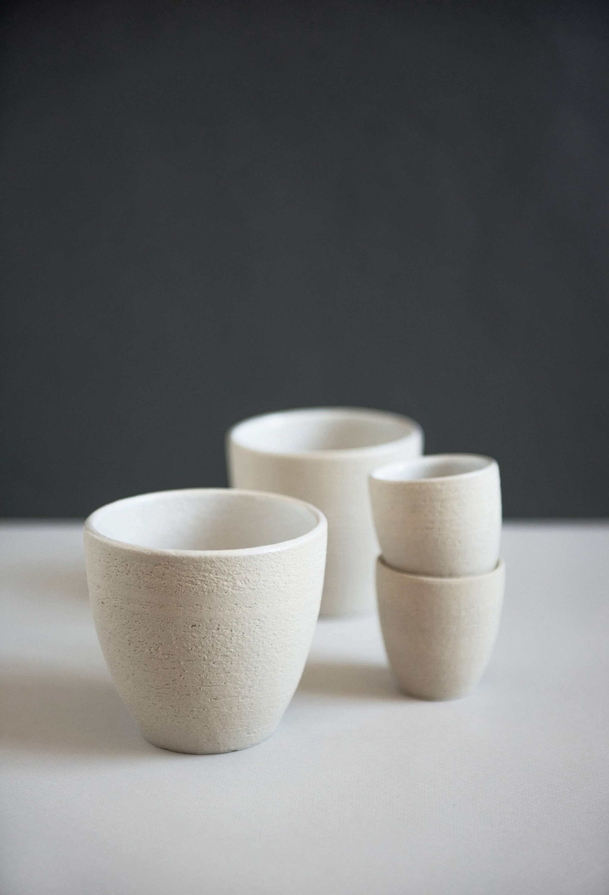Handmade Stoneware -Coffee Cup Handmade stoneware coffee cup and smaller stoneware cups on a white surface against a dark background.