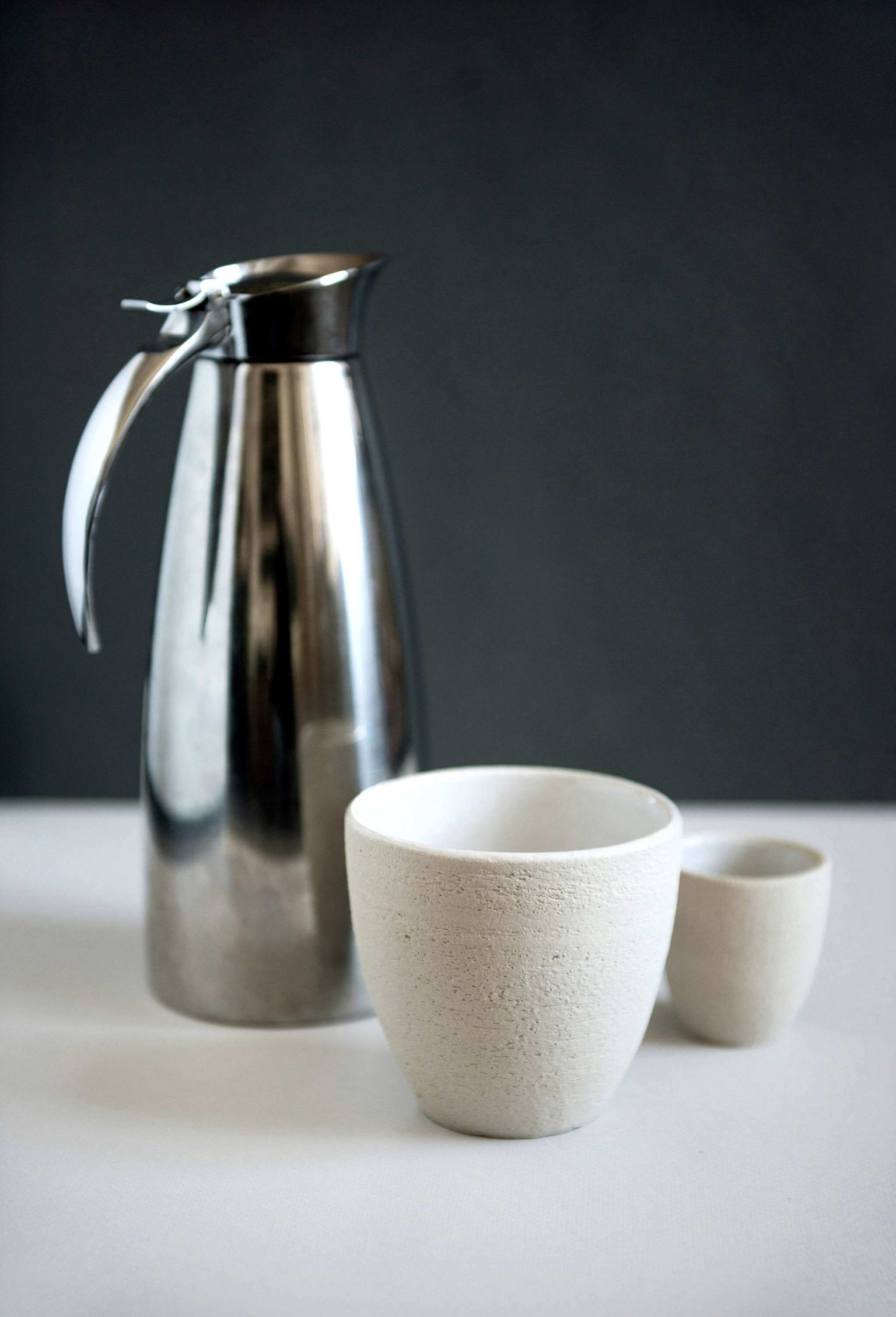 Handmade Stoneware -Coffee Cup alongside a stainless steel carafe and a smaller cup.
