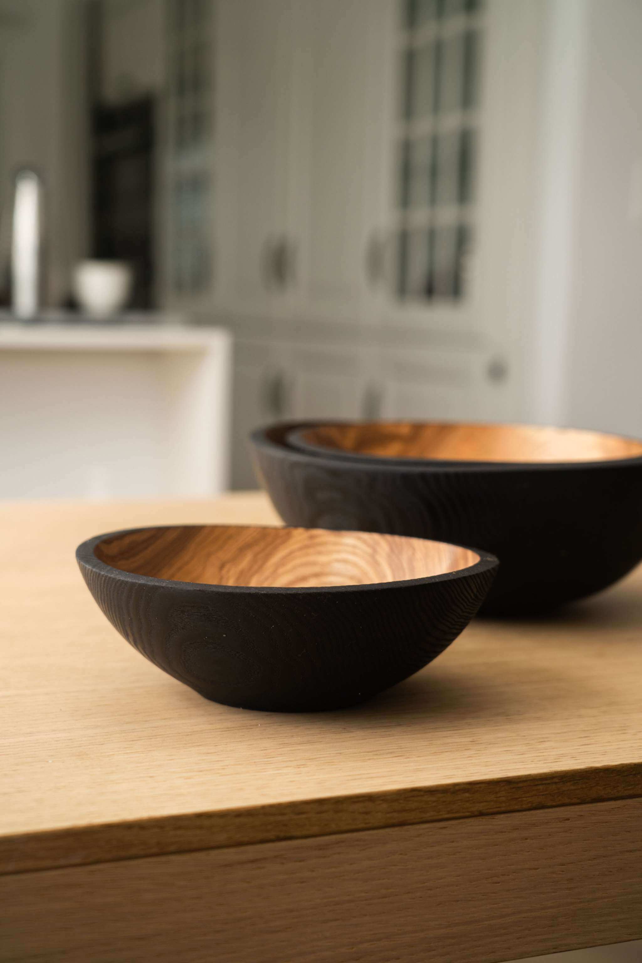 Half Charred Ashwood Nesting Bowl Set Two bowls from the charred wood nesting bowl set on a wooden table, showcasing their natural patterns.