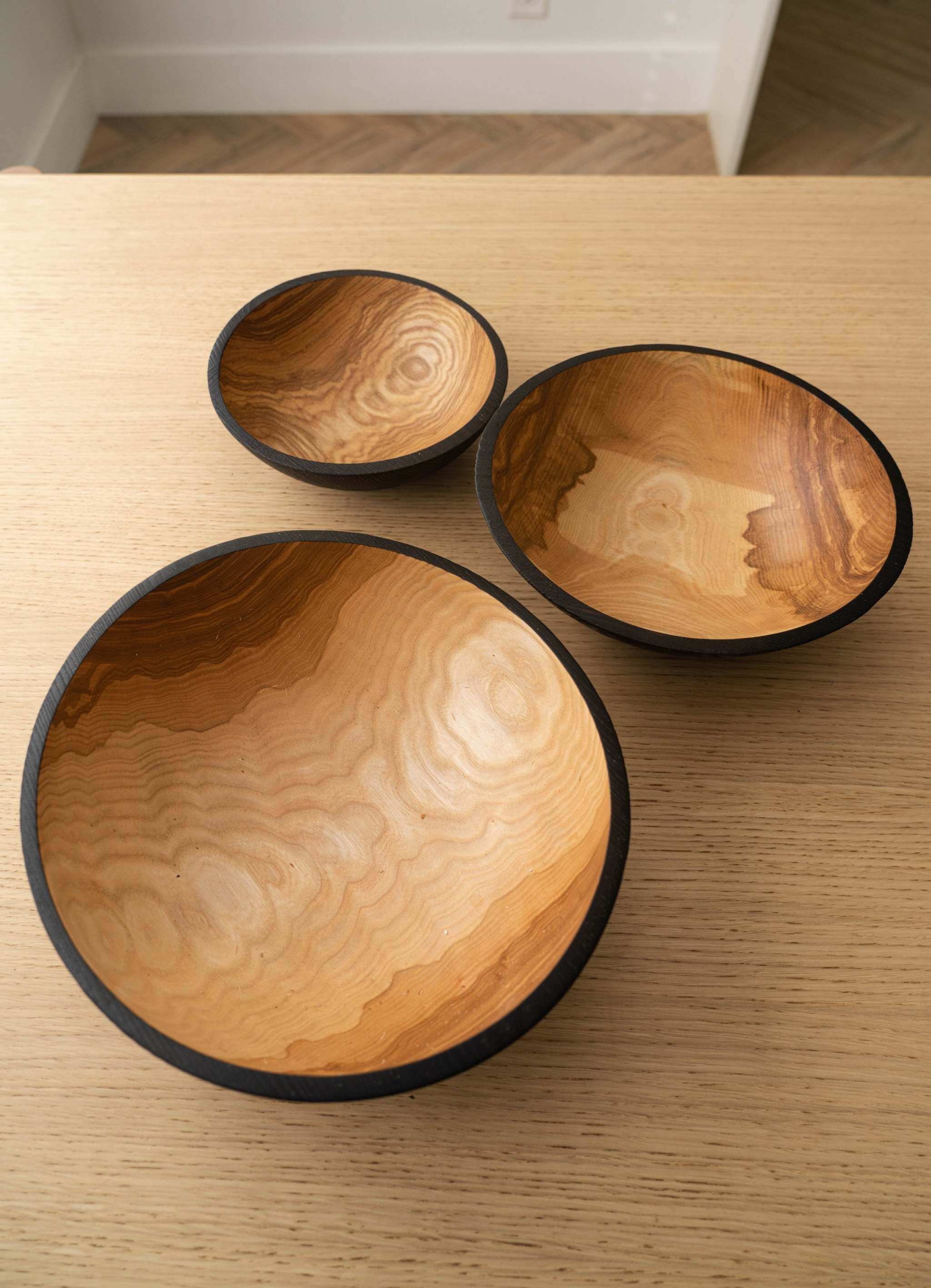 Half Charred Ashwood Nesting Bowl Set Half charred wood nesting bowl set featuring three sizes on a wooden table surface.