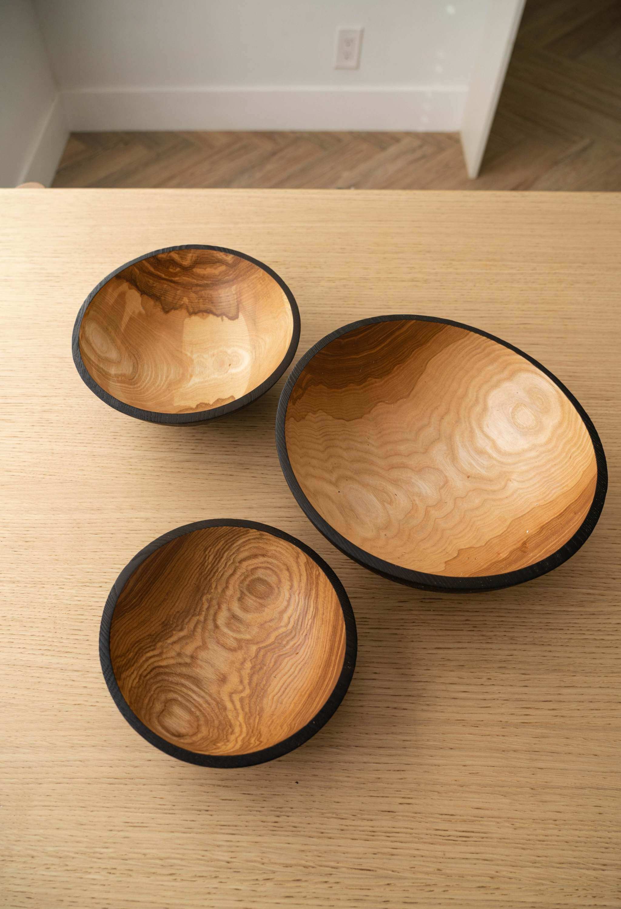 Half Charred Ashwood Nesting Bowl Set Half charred wood nesting bowl set in three sizes showcasing textured wood grain on a wooden table.