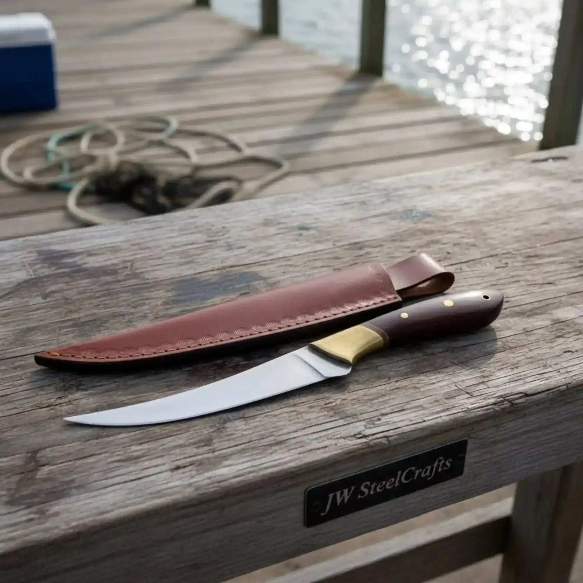 Handmade fillet knife rosewood handle resting on wooden dock with leather sheath.