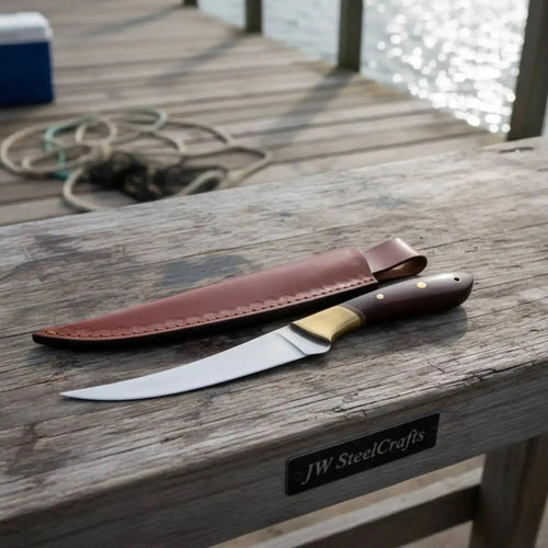 Handmade fillet knife rosewood handle resting on wooden dock with leather sheath.