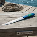 Damascus steel fillet knife with two-tone blue and green wood handle on dock surface by JW SteelCrafts.